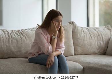 Sad lonely woman sits on sofa alone at home looks frustrated feel worried suffers from break up, having mental disorder, psychological concerns, need professional counsellor help, think about problems
