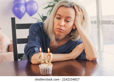 Sad lonely woman is sitting at table and looking at birthday cake. Unhappy middle age female of forty is thinking about life - Shutterstock ID 2142154817