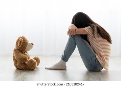 Sad long-haired little girl in casual outfit sitting with toy teddy bear and crying, feeling down, upset kid got punished after quarrel with parents, panorama with copy space, home interior