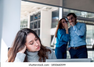 A Sad looking Turkish woman is working on desk and there are two colleagues are gossiping at background behind of her - Shutterstock ID 1850660599