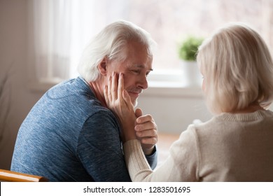 Sad loving couple wife and husband sitting together looking at each other with love, man holding hand of beloved woman, female touching male cheek. Disease or diagnosis, empathy and regret concept