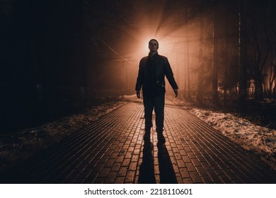 Sad man alone walking along the alley in night foggy park.