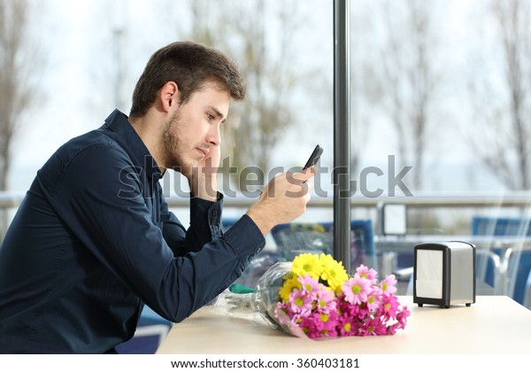 Sad man with a bouquet of\
flowers stood up in a date checking phone messages in a coffee\
shop