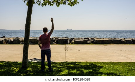 A Sad Man Or Boy Standing Alone On The Seaside And Waving His Hand To The Distant Ship With Feeling Lonely. Time To Go. Missing Someone. Desire To Go Far Away. Time To Say Goodbye. Hope To Go.