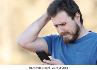 Sad man checking smart phone bad content standing outdoors