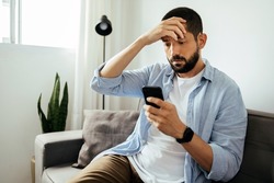 Hombre Triste Revisando Un Smartphone Sentado En Un Sofá En Casa