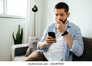 Sad Man Checking Smartphone Sitting On A Sofa At Home