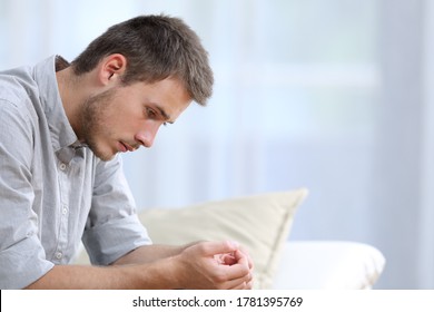 Sad man complaining looking down sitting in the sofa in the living room at home