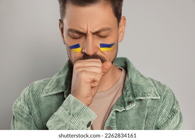 Sad man with drawings of Ukrainian flag on face against light grey background, closeup - Powered by Shutterstock