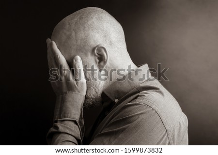 sad man with his hands closed face turned away from the light. despair and depression. shame and guilt. sadness and exile

