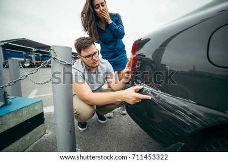 sad man looking on car scratch, woman stand behind him with sorrowful look