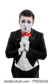 Sad Man With Prayer Hands. Studio Shot Of Male Mime Artist, Dressed In Black Suit And Wearing Red Bow Tie, Imitating Sorrow And Asking For Mercy Or Forgiveness.