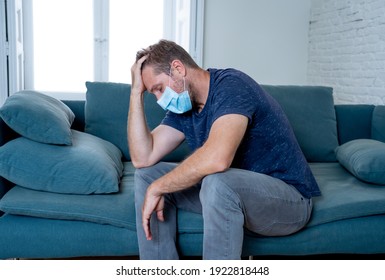 Sad man with protective face mask at home living room couch feeling tired and worried suffering depression amid coronavirus lockdown and social distancing. Mental Health and isolation concept.