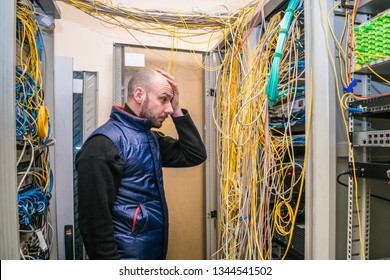 A Sad Man Put His Hand To His Face At The Sight Of Problems With Laying Wires In The Server Room. Incorrect Connection Of Communication Equipment In The Data Center. Wrong Work