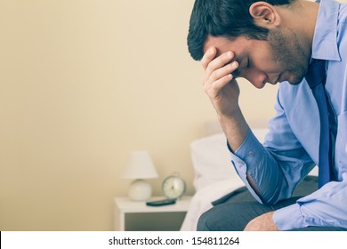 Sad Man Sitting Head In Hands On His Bed In A Bedroom At Home