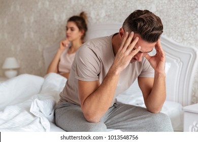 Sad Man Sitting On Bed With His Girlfriend On Background At Home