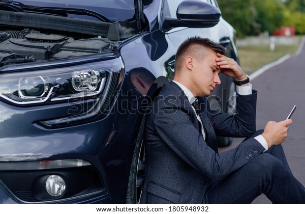 sad man use smartphone sitting on\
road near the broken car opened the hood, calling car assistance\
services, help repair stress problem emergency insurance\
aut