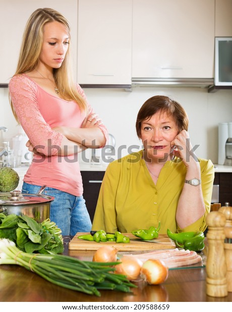 Sad mature female with daughter  sharing bad news in\
kitchen at home