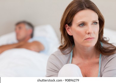 Sad Mature Woman On Bed With Her Husband In The Background