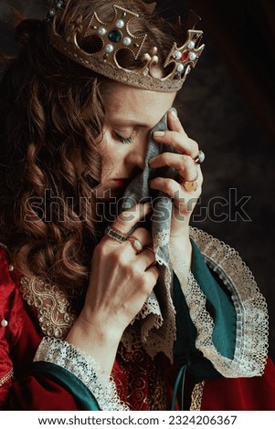 sad medieval queen in red dress with handkerchief and crown crying on dark gray background.