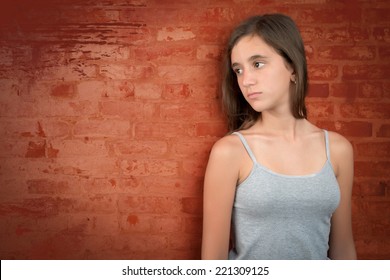 Sad and melancholic teenage girl leaning on a grunge bricks wall