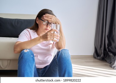 Sad Middle Aged Woman Sitting At Home On The Floor With Glass Of Water. Health Problems Of Older Women, Mental Health, Migraine Pain, Menopause Symptom, Depression Period After Coronavirus Covid-19