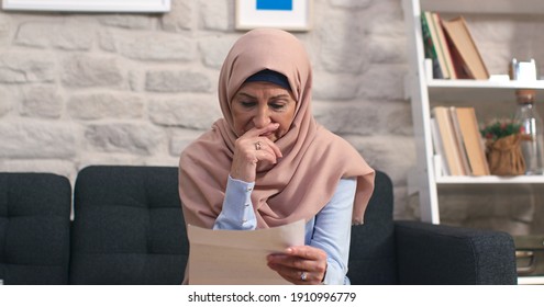 Sad Middle-aged Woman In Turban Is Reading A Letter At Her Home. The Old Woman With A Headscarf Cries At The Letter She Read And Receives Sad News.