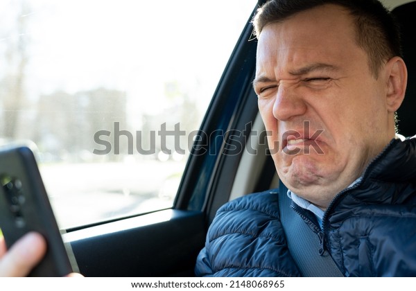 Sad\
millennial guy looks at phone screen in surprise, sits in passenger\
seat. Disgusted and overwhelmed man stares at screen of smartphone,\
needs to pay debts immediately. Heartbroken man\
