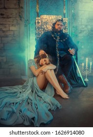 Sad Miserable Offended Woman Queen Victim Of Dictator Domineering Man. Power King In Golden Crown Sits On Iron Throne Inside Castle Medieval Old Room. Luxury Royal Clothing. Romantic Scandal Quarrel