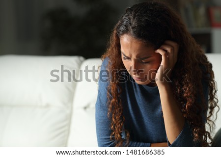 Sad mixed race woman complaining sitting on a couch in the living room at home