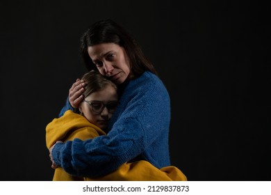 Sad mother hugging her daughter, both wearing Ukrainian national colors on black background. - Shutterstock ID 2129837873