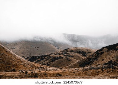sad mountains in a desolate landscape without trees and with some bushes with low clouds on the summit and a gloomy gray sky without the sun's rays, mount cook, new zealand