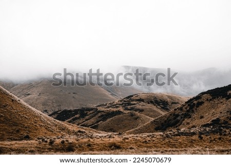 sad mountains in a desolate landscape without trees and with some bushes with low clouds on the summit and a gloomy gray sky without the sun's rays, mount cook, new zealand
