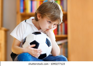 Sad And Not Happy Little Kid With Football About Lost Football Or Soccer Game. Child After Watching Match On Tv