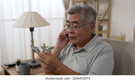 Sad old asian man with credit card call bank support by cellphone reporting about money fraud. senior male telling problem on smartphone while taking debit card. elderly grandpa talk on mobile phone - Shutterstock ID 2245453073