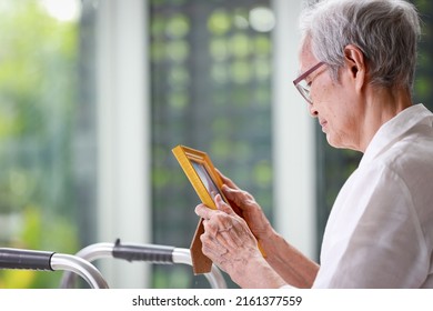 Sad Old Elderly With Depression Looks At Photograph Of Her Family With Nostalgia,remembrance,Depressed Asian Senior Woman Patient Holding Picture Frame,sitting Alone In Loneliness At Nursing Home