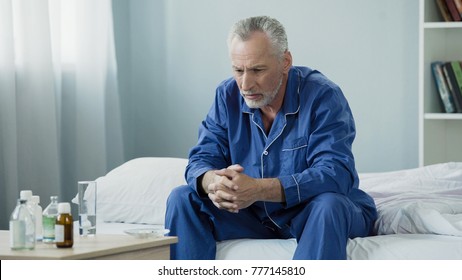 Sad Old Man Sitting In Bed And Looking At Pills, Medication And Healthcare