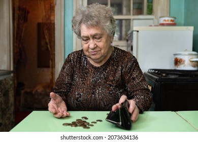 A Sad Old Woman Counts Money At Home In The Kitchen. The Concept Of Poverty, Old Age, Poor Lifestyle Of The Elderly. 