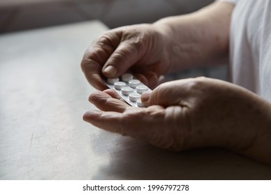 Sad Old Woman Taking Pills, Health Problems In Old Age, Expensive Medications. An Elderly Woman's Hands Unpacking Several Pills For Taking Medication. Grandma Takes Tablet And Drinks A Glass Of Water