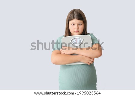Sad overweight girl with measuring scales on light background