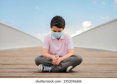 Sad And Pensive Kid With Protective Surgical Mask Sitting On The Floor Outdoor