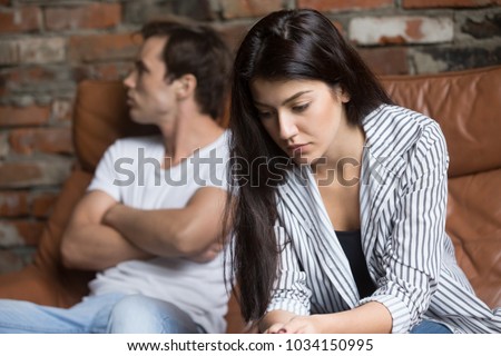 Sad pensive young girl thinking of relationships problems sitting on sofa with offended boyfriend, conflicts in marriage, upset couple after fight dispute, making decision of breaking up get divorced