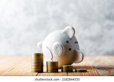 A sad piggy bank behind stacks of euro coins symbolizing the fall of monetary assets. White moneybox with coins graph. Crisis concept - Shutterstock ID 2182844533