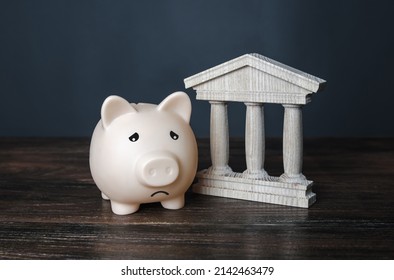 Sad piggy bank and state building. crisis, depletion of savings and bankruptcy. Financial default. Devaluation, inflation. Impoverishment. Refinancing and restructuring of debts. Insolvency - Shutterstock ID 2142463479