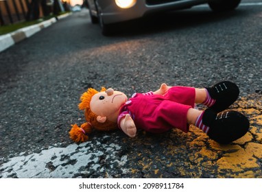 A sad plush toy doll is lying on the road near the wheel of a car. The concept of a road traffic accident.