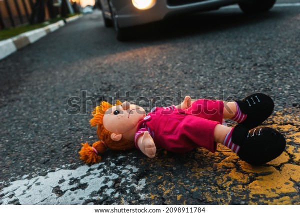A sad plush toy\
doll is lying on the road near the wheel of a car. The concept of a\
road traffic accident.