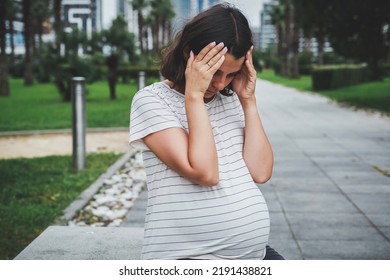 a sad pregnant woman sits alone on a bench in the park in summer - Powered by Shutterstock