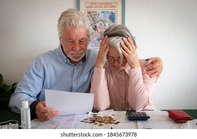 A Sad Retired Senior Couple Comes To Terms With The Economic Impact Of The COVID-19 Coronavirus On Their Financial Possibilities. They Watch The Bills To Pay By Hugging Each  To Give Themselves Streng