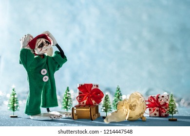 Sad Santas Helper Elf With Head In Hands Standing Next To A Broken Christmas Bauble. North Pole Christmas Scene. Santas Workshop. Elf At Work.