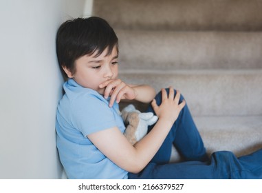 Sad School kid sitting alone on staircase in the morning, Lonely boy looking dow with sad face not happy to go back to school, Depressed child boy sitting in the corner of a stair,Mental health
